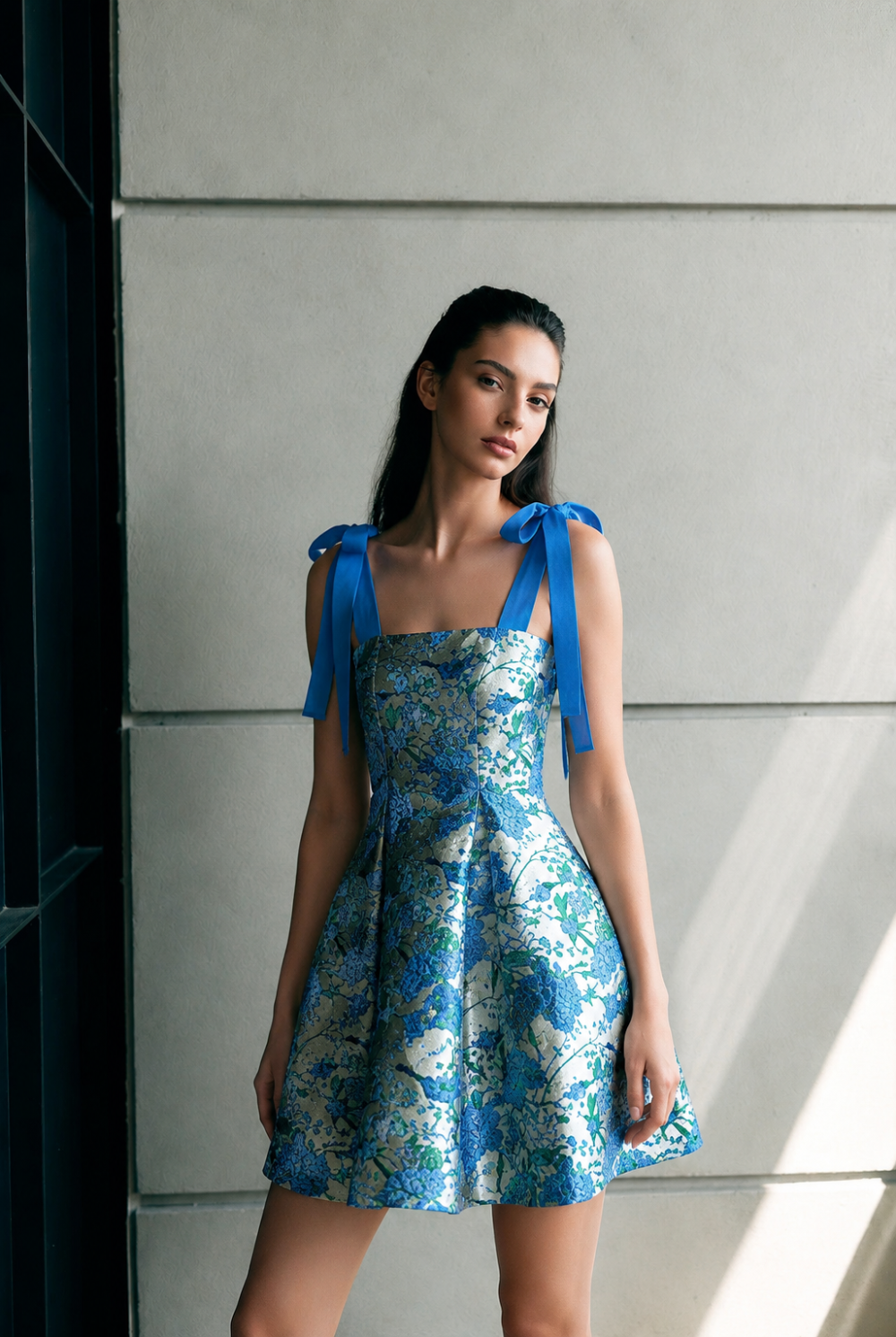 Model wearing the Dina Floral Jacquard mini dress in blue, featuring bright blue ribbon tie-straps.