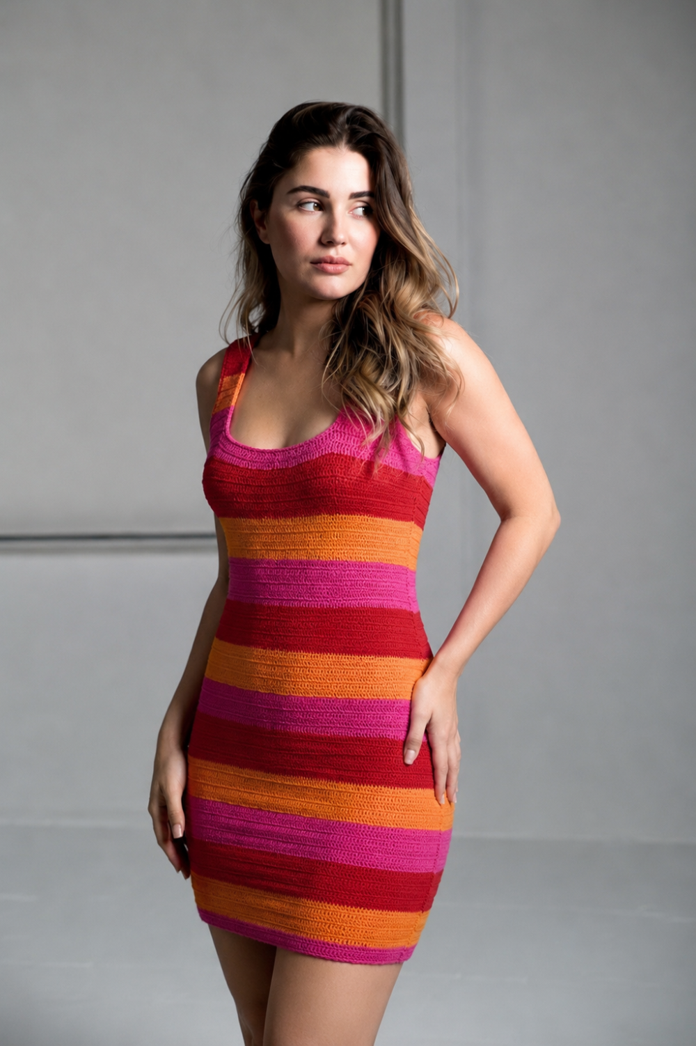Model wearing the MUMU Day Trip dress, a vibrant pink, red, and orange striped knit mini dress.